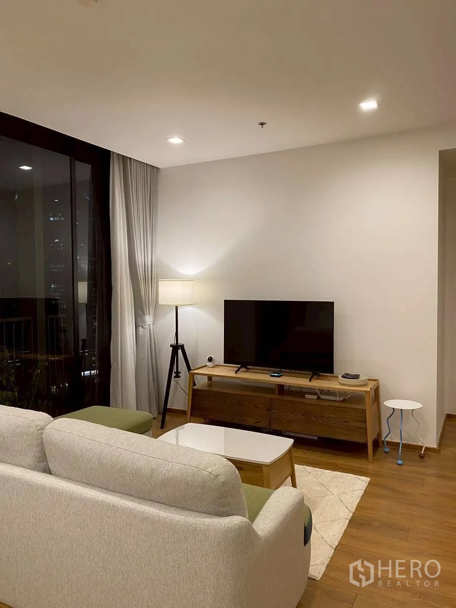 Condominium for rent in Watthana, Bangkok - TV area at night with tripod floor lamp and large window.