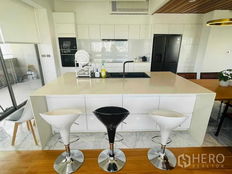 คอนโด ให้เช่าหรือขายในWatthana, Bangkok - ไอแลนด์ครัวสีขาวพร้อมอ่างล้างและสตูลสามตัว ข้างโต๊ะทานข้าวและตู้เย็นสีดำ