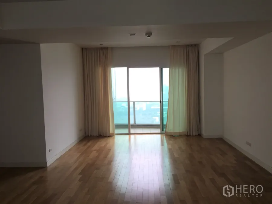 คอนโด ให้เช่าในKhlong Toei, Bangkok - ห้องนั่งเล่นกว้างพื้นไม้ ผ้าม่านโปร่ง ประตูบานเลื่อนออกสู่ระเบียงชมวิวสกายไลน์กรุงเทพฯ