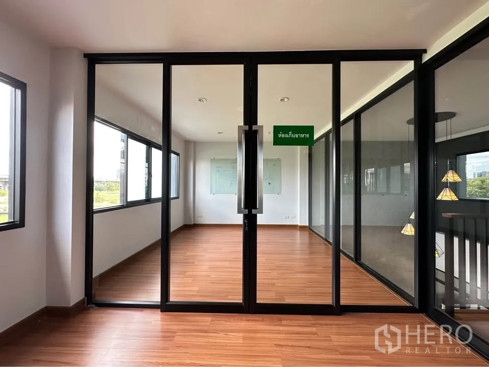 Townhouse for rent in Pak Kret, Nonthaburi - Glass-partitioned multipurpose room with wood floors and surrounding windows.