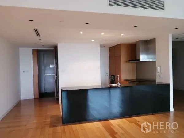 Condominium for sale in Yan Nawa, Bangkok - Open-plan kitchen with black stone island, wood flooring and recessed lights.
