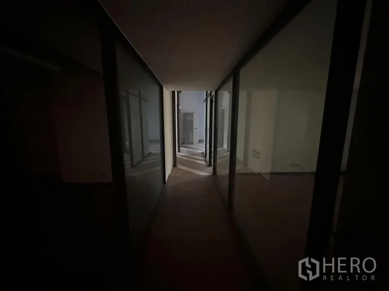 Office Space for rent in Khlong Toei, Bangkok - Narrow corridor lined with glass-partitioned rooms leading toward natural light.