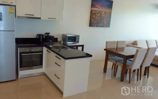 Condominium for sale in Bang Lamung, Chon Buri - Modern white kitchen with oven, refrigerator and four-seat dining table in an open-plan layout.