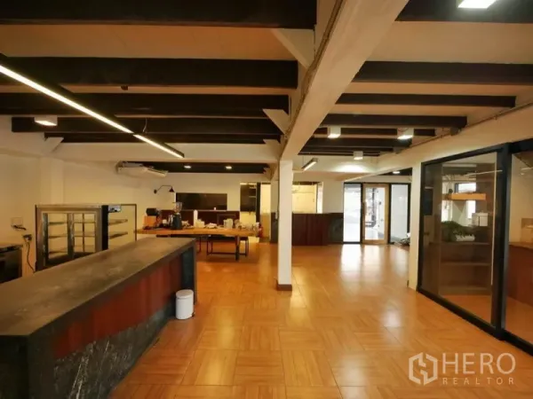 พื้นที่ขายปลีก ให้เช่าในKhlong Toei, Bangkok - ภายในร้านกว้าง เคาน์เตอร์หินยาว ไฟเพดานเส้นยาว ผนังกระจก และพื้นโทนอุ่น.