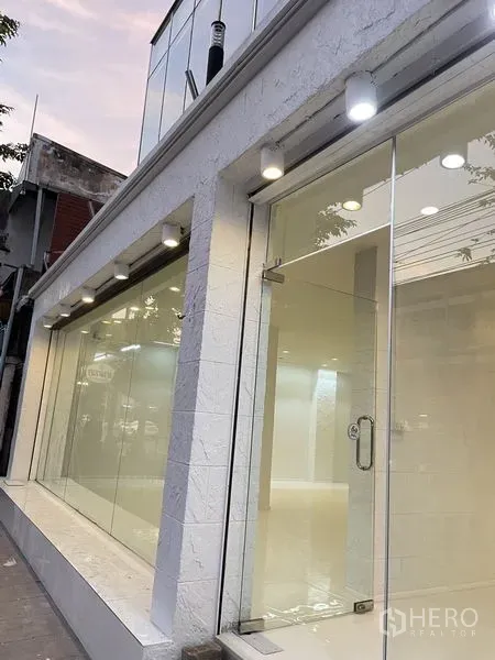Shophouse for rent in Dusit, Bangkok - Modern white shophouse exterior with floor‑to‑ceiling glass windows and spotlights at dusk in Dusit, Bangkok.