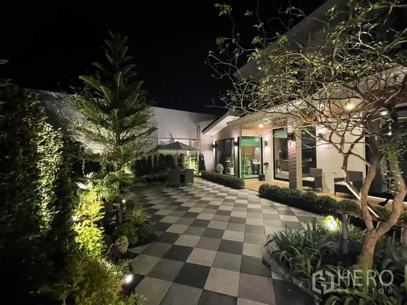 Detached House for rent in Phasi Charoen, Bangkok - Illuminated courtyard at night with trees, hedges and tiled walkway.