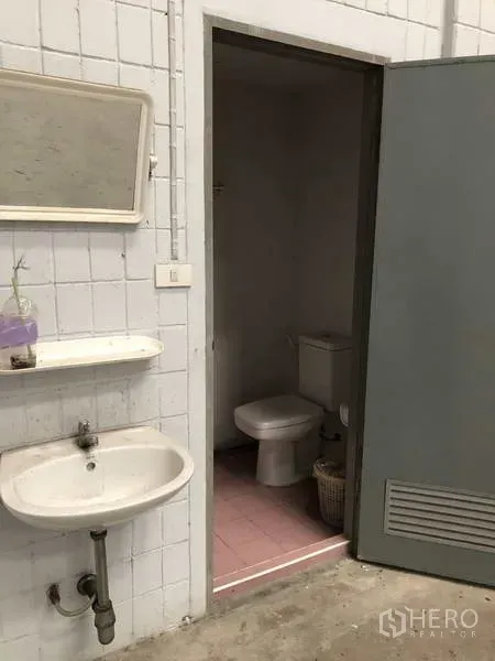 Warehouse for rent in Lat Lum Kaeo, Pathum Thani - Industrial washroom entrance with a wall-mounted sink and mirror beside a toilet room.