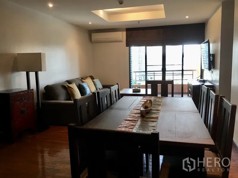 Condominium for rent in Pathum Wan, Bangkok - Open-plan living and dining room with wooden floors, sofa set, dining table, and balcony access.