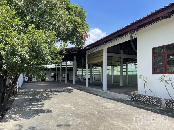 工厂 出租或出售在Pathum Thani - 半开放式厂棚，高柱林立，旁侧为围墙与树木。