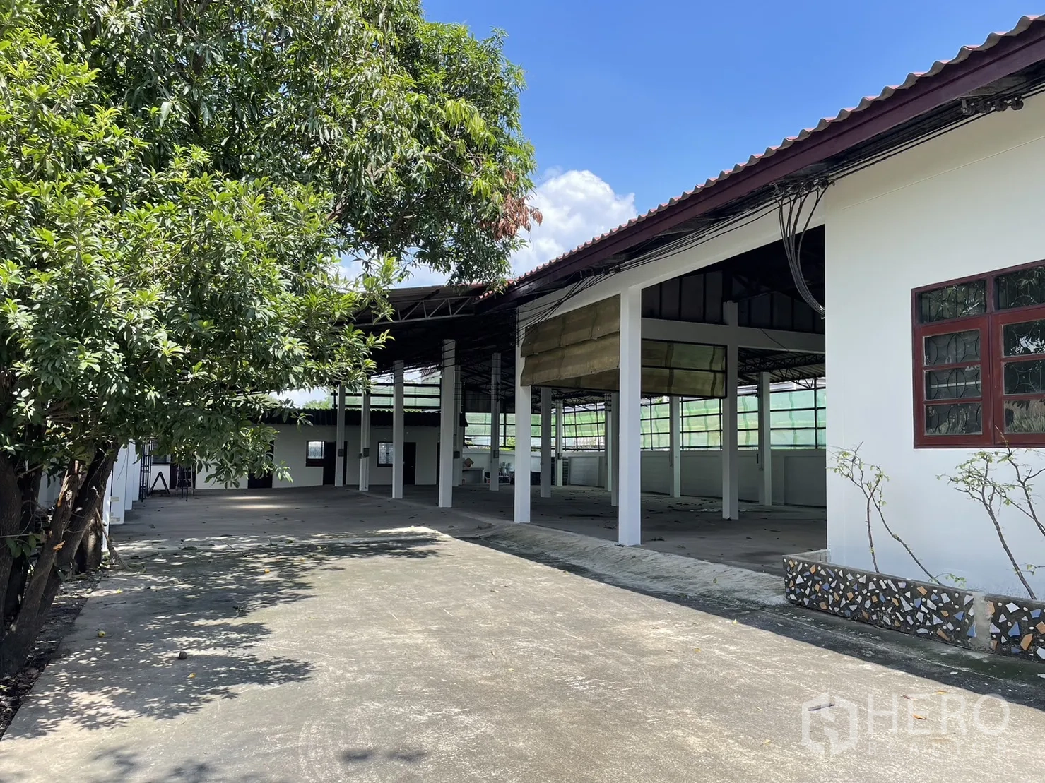 工厂 出租或出售在Pathum Thani - 半开放式厂棚，高柱林立，旁侧为围墙与树木。