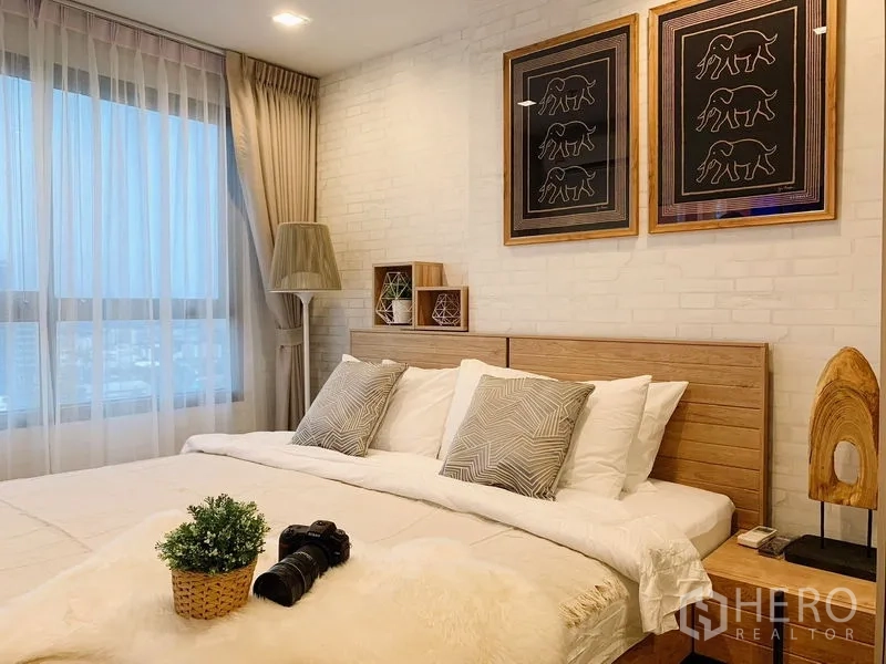 公寓 出租或出售在Phra Khanong, Bangkok - 温馨卧室，大窗与窗帘、木质床头板及城市风格装饰画。