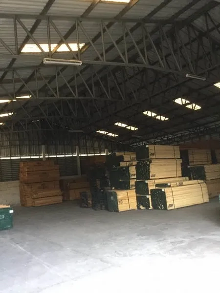 Warehouse for sale in Sai Noi, Nonthaburi - Spacious storage hall with skylights and timber stacks for inventory.