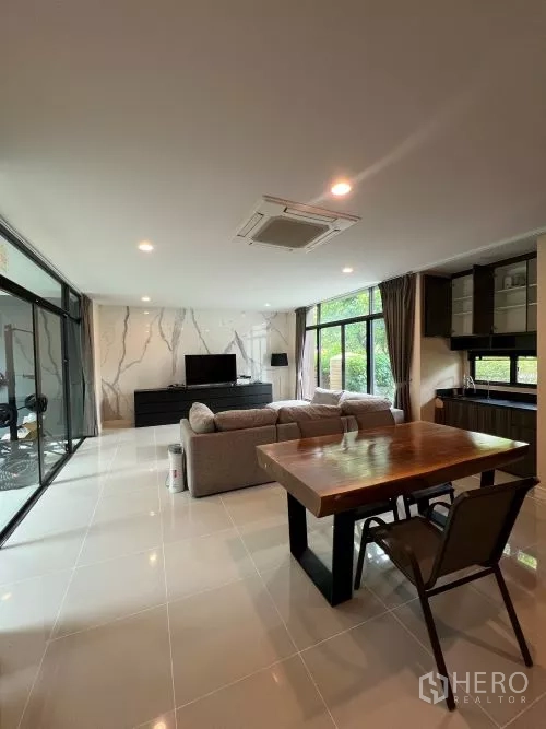 独立式住宅 出租在Bang Kapi, Bangkok - 开放式客餐厅，大理石纹背景墙、电视柜、木餐桌与推拉玻璃门。