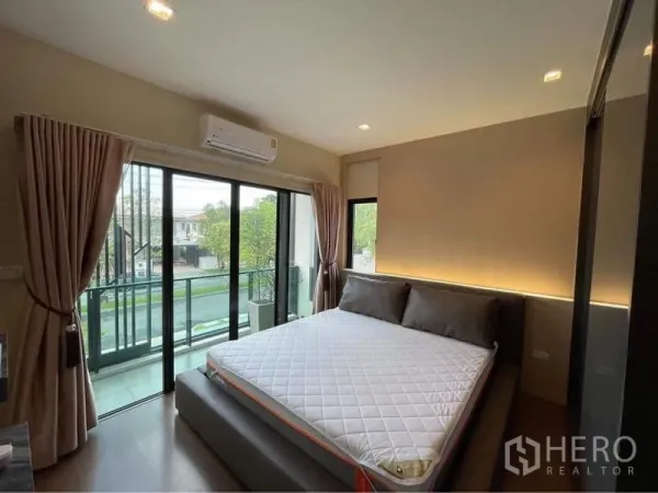 Detached House for rent or sale in Bang Phli, Samut Prakan - Bedroom opening to a glass balcony through sliding doors with green neighborhood views.