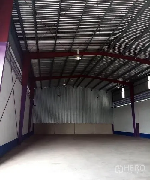 Warehouse for rent in Pathum Thani - Deep view of empty warehouse bay showing long-span steel beams, insulated metal roof, and open floor space.