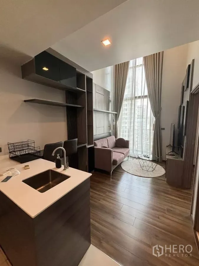 Condominium for rent or sale in Watthana, Bangkok - Open-plan living with double-height ceiling, kitchen island and floor-to-ceiling windows in an Ekkamai condo.
