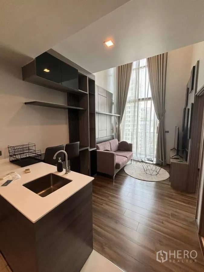 Condominium for rent or sale in Watthana, Bangkok - Open-plan living with double-height ceiling, kitchen island and floor-to-ceiling windows in an Ekkamai condo.