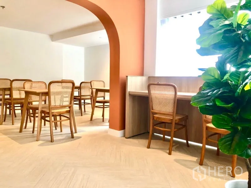 Office Space for rent in Khlong Toei, Bangkok - Co-working zone with multiple wooden tables, a study counter by the window, arched feature wall and indoor plant.