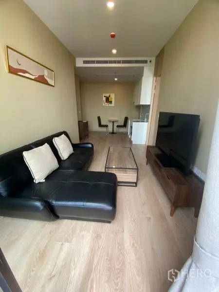 คอนโด ให้เช่าในWatthana, Bangkok - ห้องนั่งเล่นแปลนเปิด โซฟาหนังสีดำ ตู้วางทีวี และพื้นไม้โทนอ่อน