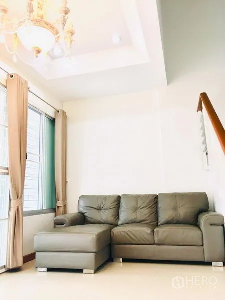 联排别墅 出租在Prawet, Bangkok - 舒适沙发角，L形皮沙发、窗户与吊灯。