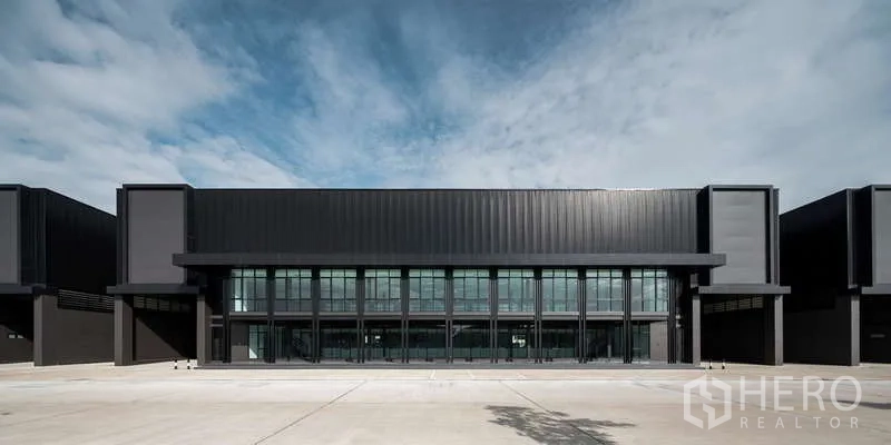 คลังสินค้า ให้เช่า - อาคารโกดังสีดำสมัยใหม่ ด้านหน้าเป็นกระจกเต็มผนัง พร้อมลานโหลดกว้างใต้ท้องฟ้าใส