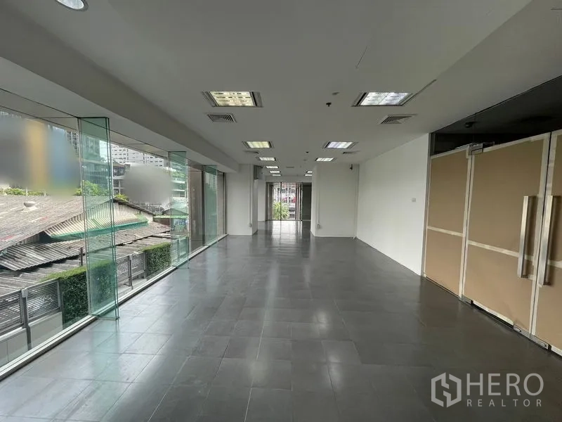 สำนักงาน ให้เช่า - สำนักงานแบบเปิดโล่ง มีกระจกสูงจรดเพดาน พื้นกระเบื้องสีเทา และไฟฝ้าทีบาร์