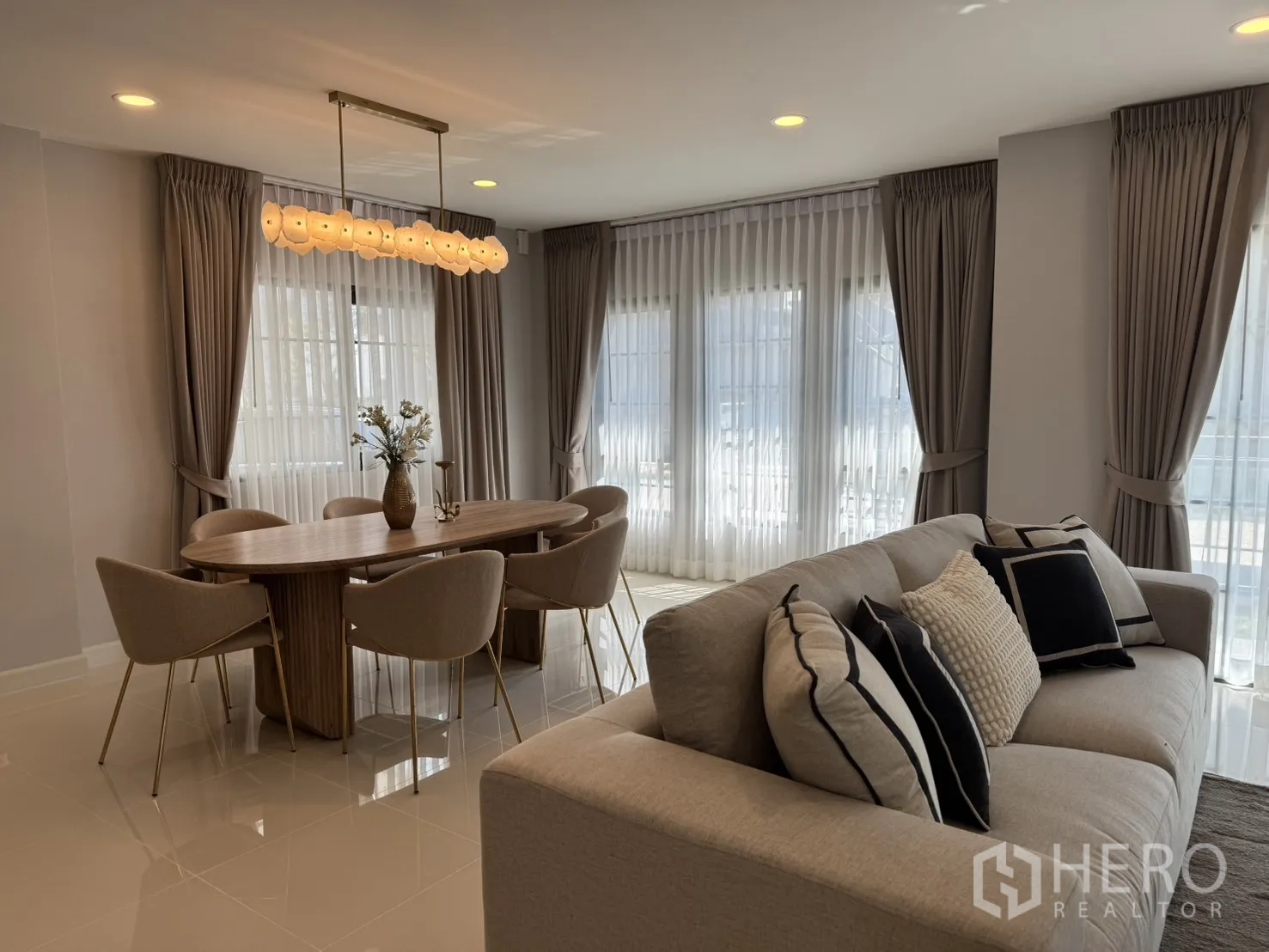 Detached House for rent in Bang Phli, Samut Prakan - Open-plan living and dining area with beige sofa, oval wooden table, pendant light and large windows.