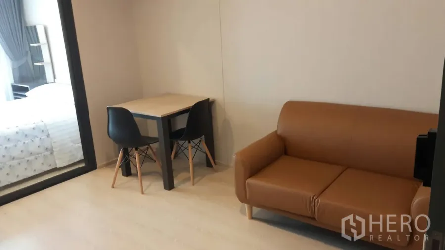 Condominium for rent in Samut Prakan - Bright living area with tan leather sofa, two-seat dining table, and glass partition to the bedroom in a Mueang Samut Prakan condo.