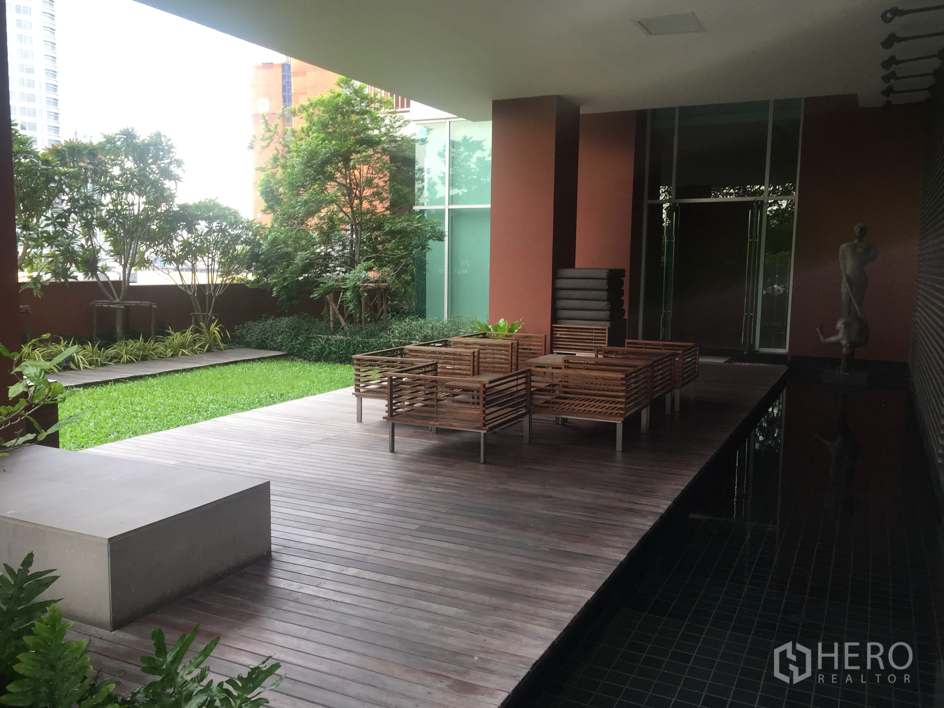 Condominium for rent or sale in Watthana, Bangkok - Covered outdoor lounge deck with wooden seating beside a landscaped garden in a Bangkok condo.