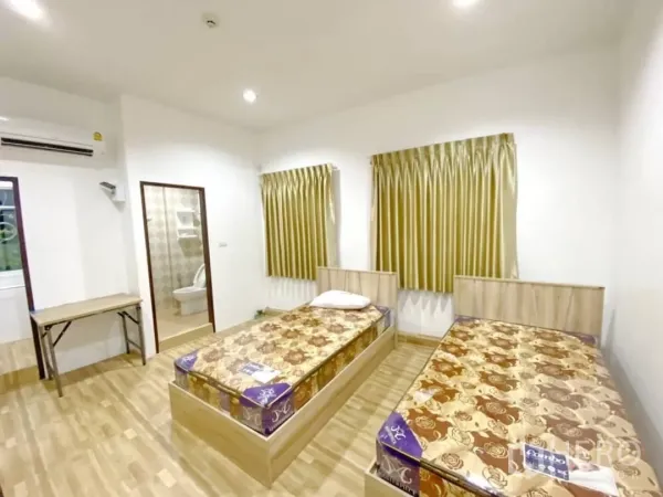 Apartment for sale in Khlong Toei, Bangkok - Bright twin-bed room with wood floors, gold curtains, a desk and an en‑suite bathroom.