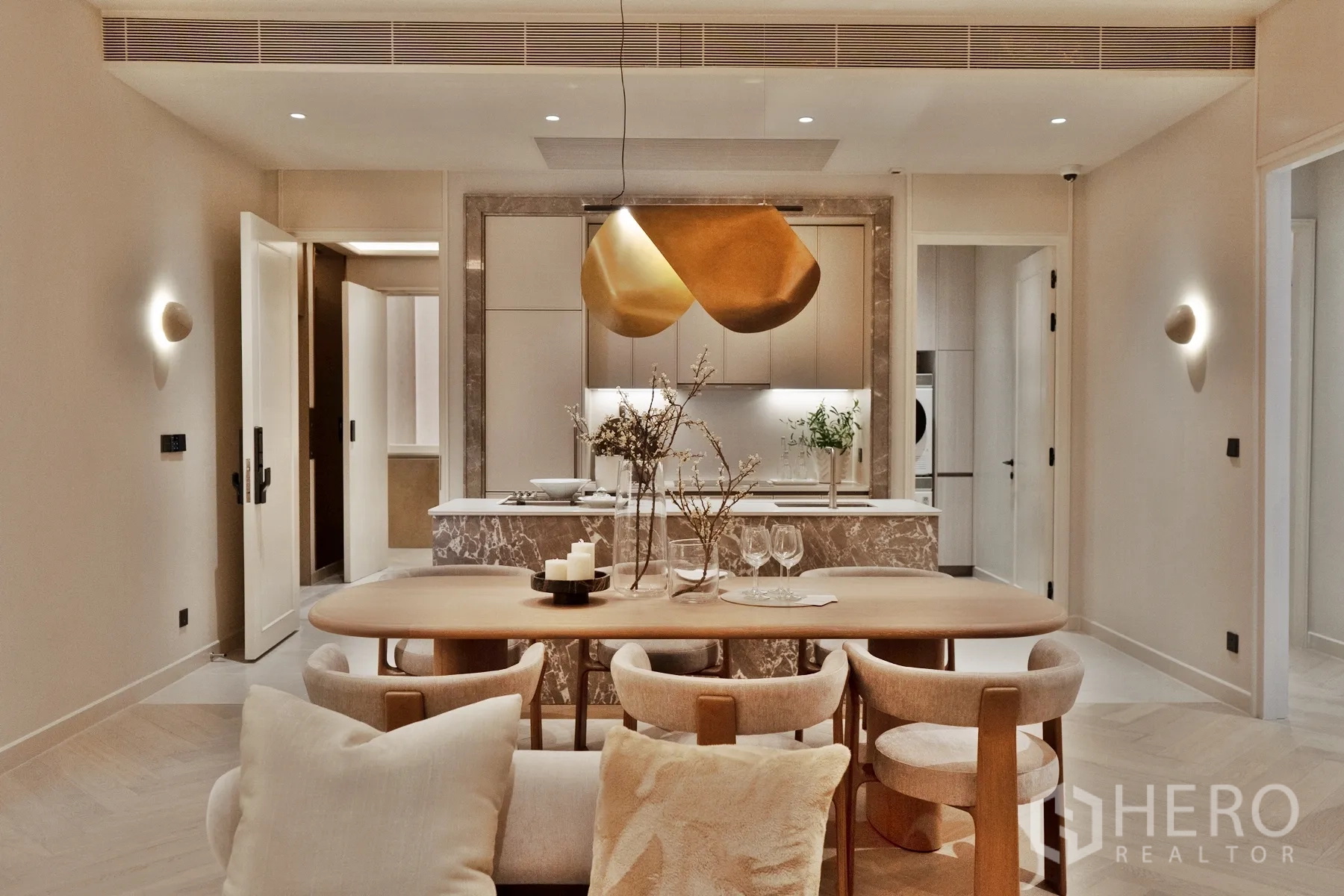 Condominium for sale in Khlong Toei, Bangkok - Warm-toned open-plan dining area with a marble island kitchen, sculptural gold pendant light, built-in cabinetry, and soft wall sconces.