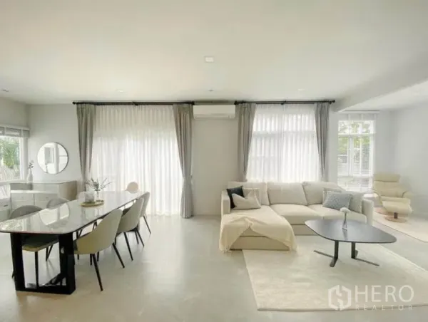 Detached House for rent in Prawet, Bangkok - Bright open-plan living and dining area with large windows, curtains and an L-shaped sofa.