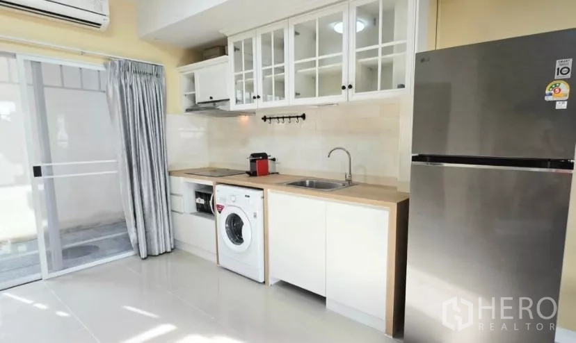 Townhouse for rent in Bang Bo, Samut Prakan - Modern white kitchen with cabinets, hob, hood, washing machine and fridge.