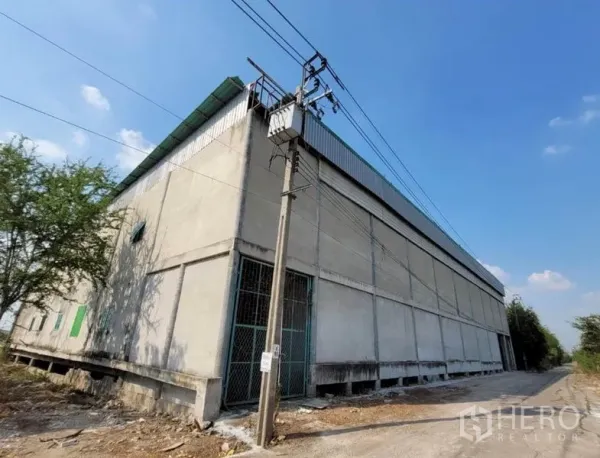 货栈 出租或出售在Sai Noi, Nonthaburi - 赛诺伊大型混凝土仓库外角，绿色屋顶，电线与侧边通道。