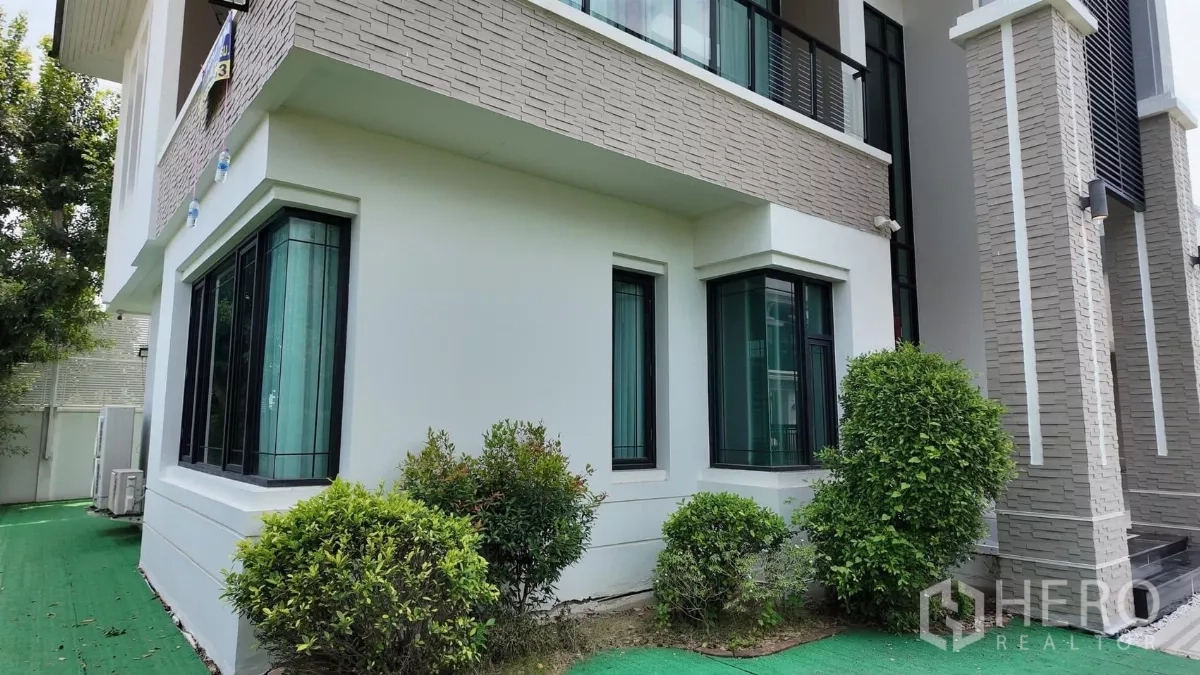 Detached House for rent in Bang Bon, Bangkok - Side garden with shrubs around the white modern house facade.