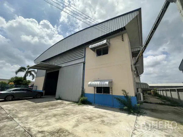 Factory for rent in Pathum Thani - Side view of metal-clad factory with high loading door, awnings and paved parking apron.