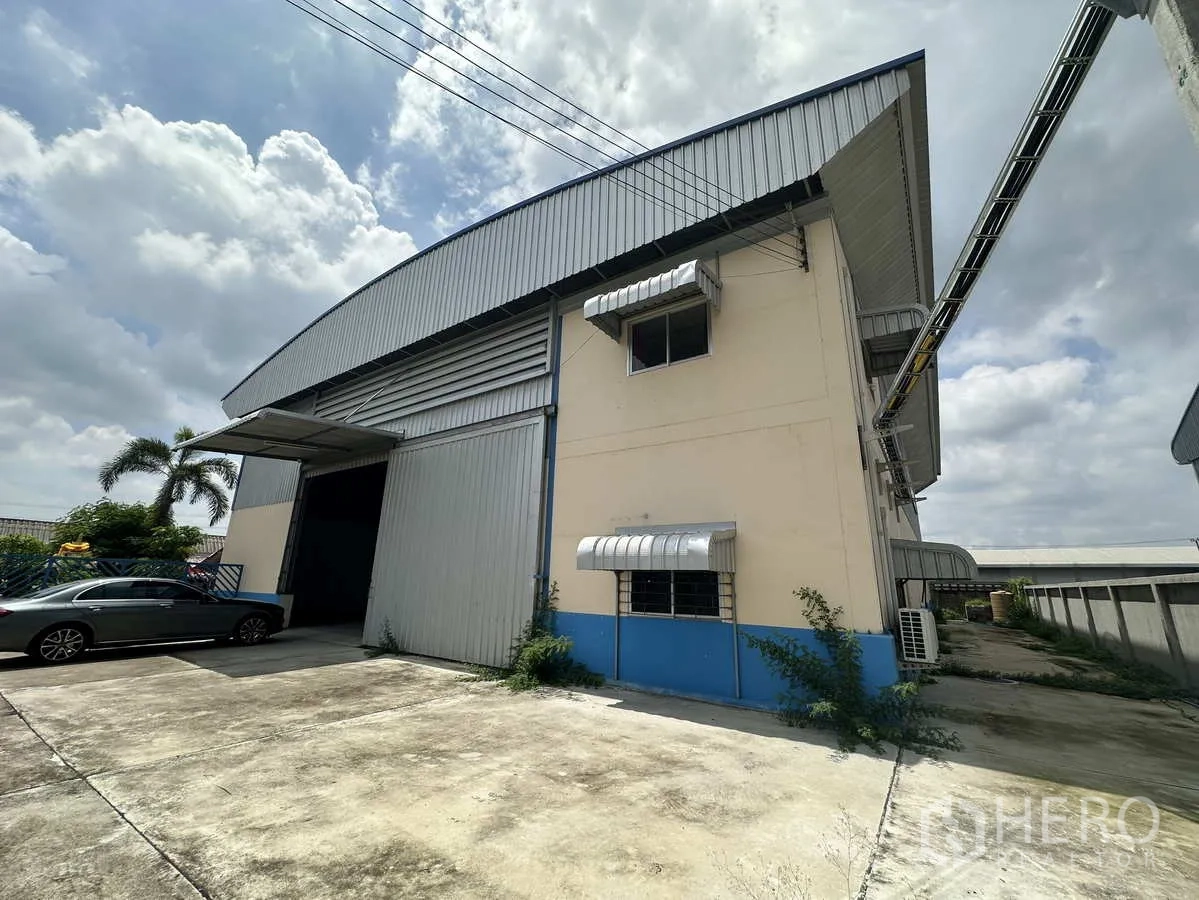 Factory for rent in Pathum Thani - Side view of metal-clad factory with high loading door, awnings and paved parking apron.