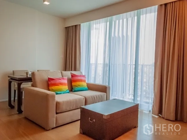 Condominium for rent in Watthana, Bangkok - Bright living room with sofa, colorful cushions, dining set, and floor-to-ceiling windows opening to a balcony.