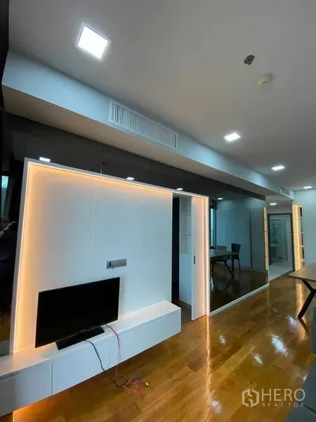 คอนโด ให้เช่าหรือขายในKhlong Toei, Bangkok - พื้นที่นั่งเล่นสมัยใหม่ ผนังทีวีพร้อมไฟเส้น LED อุ่น ๆ ข้างตู้เงาดำและประตูกระจกบานเลื่อน