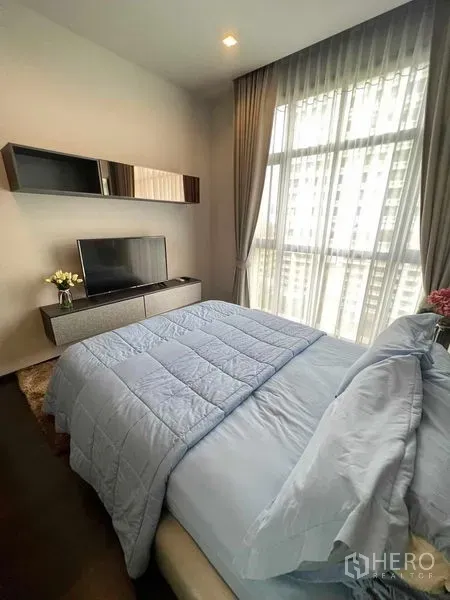 คอนโด ให้เช่าหรือขายในWatthana, Bangkok - ห้องนอนสว่าง ผ้าม่านทึบและโปร่ง ทีวีบนตู้คอนโซล พร้อมผ้าคลุมเตียงสีน้ำเงินและวิวเมือง