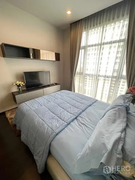 คอนโด ให้เช่าหรือขายในWatthana, Bangkok - ห้องนอนสว่าง ผ้าม่านทึบและโปร่ง ทีวีบนตู้คอนโซล พร้อมผ้าคลุมเตียงสีน้ำเงินและวิวเมือง