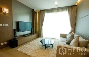 คอนโด ให้เช่าในKhlong Toei, Bangkok - ห้องนั่งเล่นสว่างพร้อมทีวีติดผนัง ชุดวางทีวี พรมขนฟู และโต๊ะกาแฟกลมข้างหน้าต่างบานใหญ่