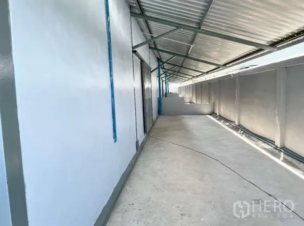 货栈 出租在Krathum Baen, Samut Sakhon - 仓库侧部带顶棚的通道与白色墙面，结构整齐。