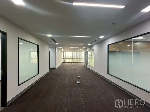 Office Space for rent - Long open-plan corridor with carpet flooring, glass-partitioned rooms and LED lights.