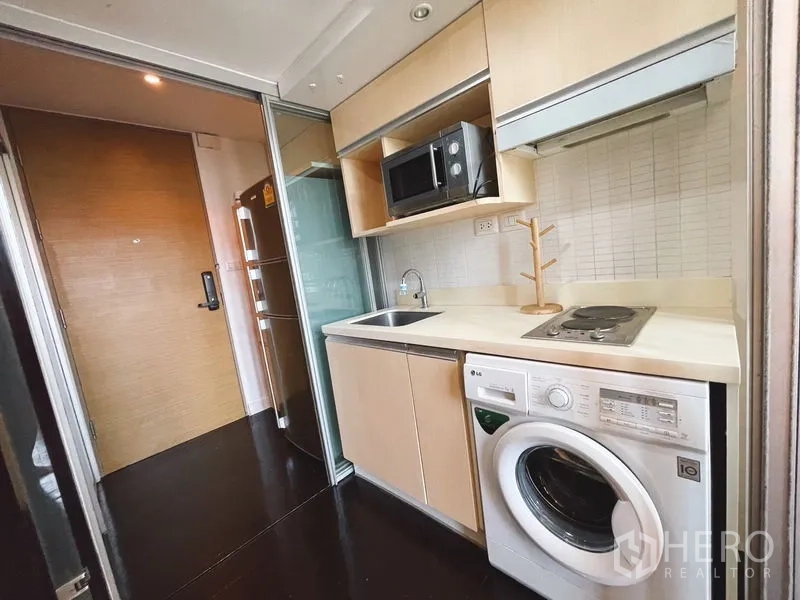 公寓 出租或出售在Khlong Toei, Bangkok - 现代一字型厨房，浅木柜、灶台、水槽、微波炉与滚筒洗衣机。