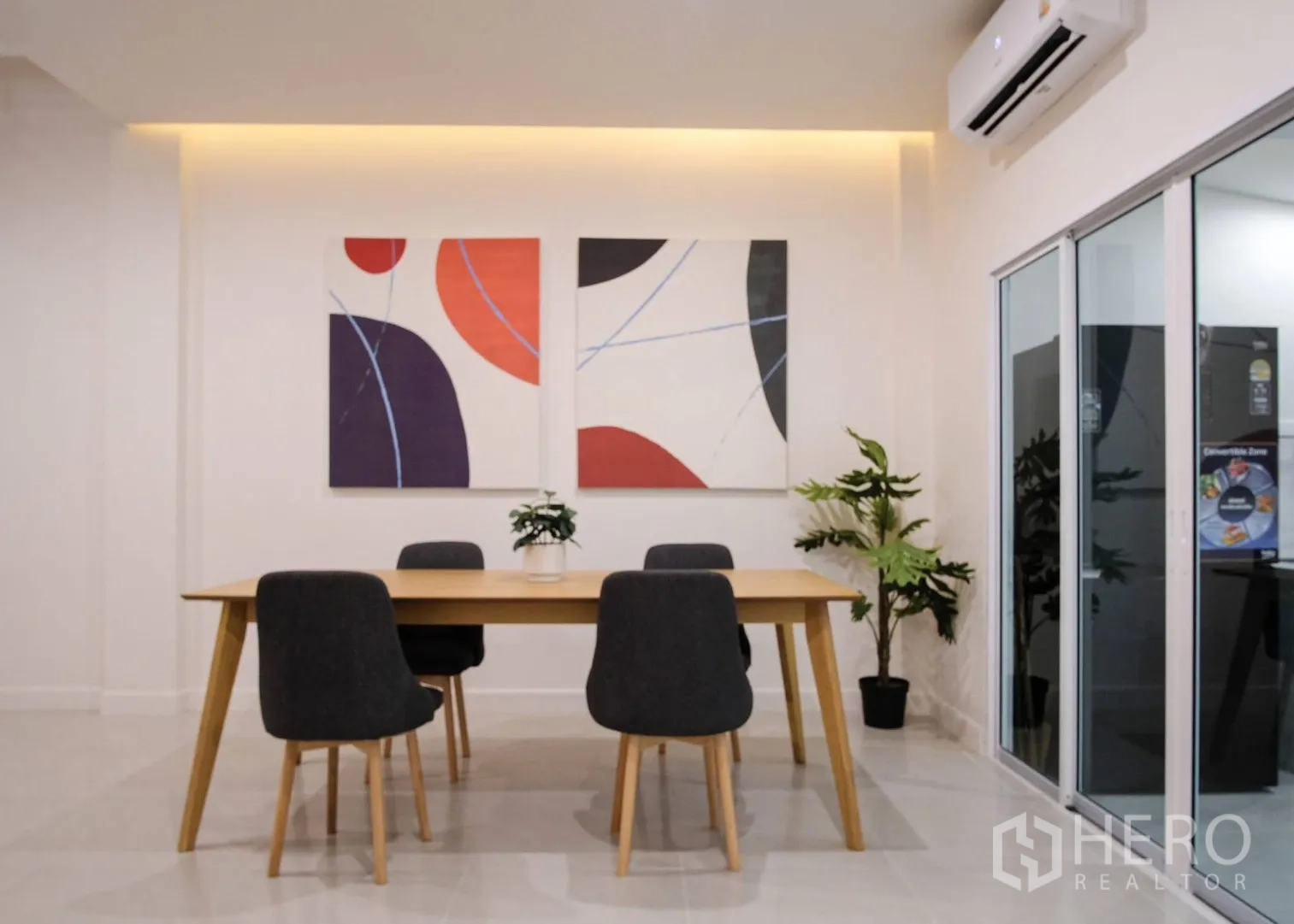 Townhouse for rent in Bang Phli, Samut Prakan - Dining room with wooden table, four upholstered chairs, artwork, and air conditioner.