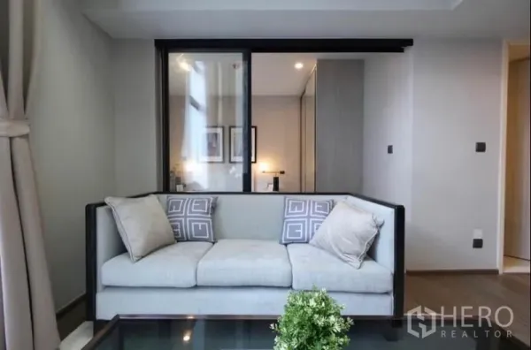 คอนโด ให้เช่าในPathum Wan, Bangkok - โซฟาใกล้ฉากกั้นกระจกบานเลื่อนเชื่อมห้องนอนในคอนโดสมัยใหม่