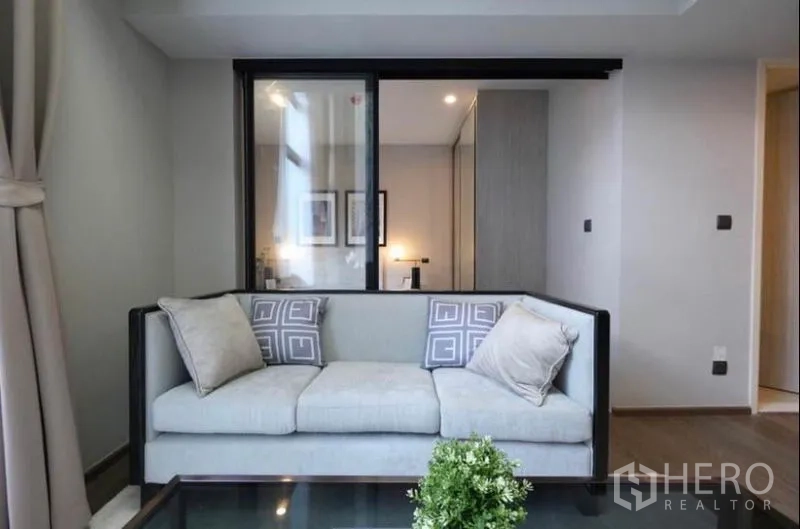 คอนโด ให้เช่าในPathum Wan, Bangkok - โซฟาใกล้ฉากกั้นกระจกบานเลื่อนเชื่อมห้องนอนในคอนโดสมัยใหม่