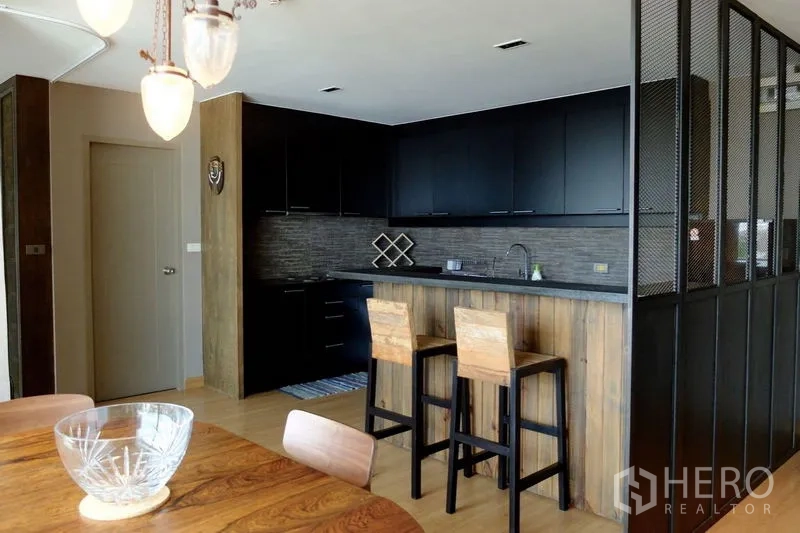 Condominium for sale in Watthana, Bangkok - Open-plan kitchen with matte black cabinets, wood breakfast bar and pendant lights beside the dining table.