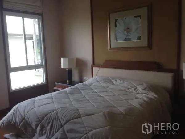 คอนโด ให้เช่าในWatthana, Bangkok - ห้องนอนมีแสงธรรมชาติ หน้าต่างบานใหญ่ เตียงหัวบุผ้า โต๊ะข้าง และภาพดอกไม้ ในคอนโดกรุงเทพฯ